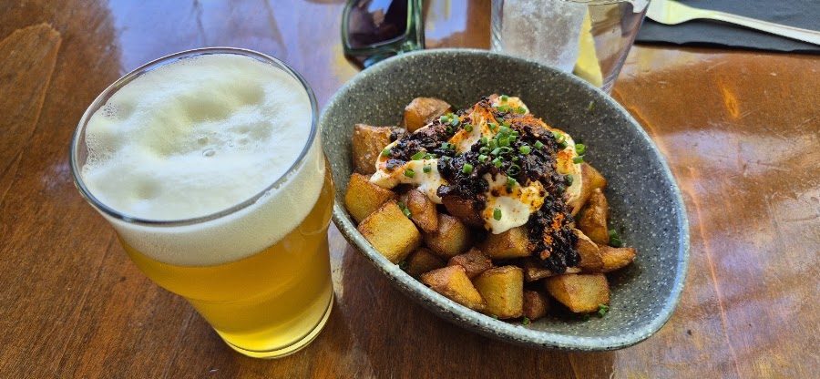 Caña de cerveza y bravas de la casa con alioli sobre una mesa de madera